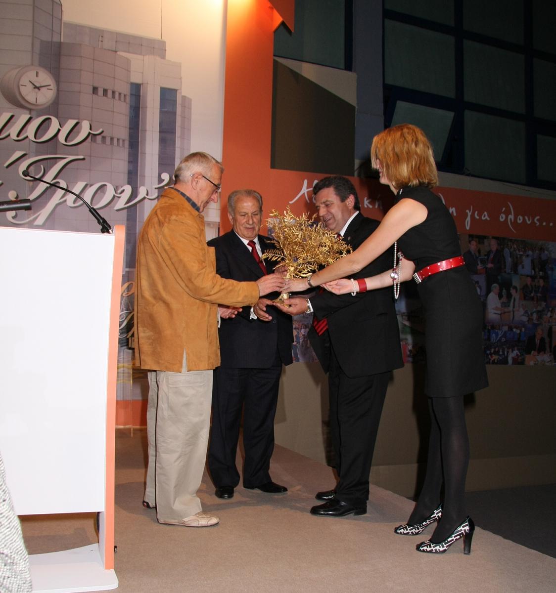 Ο Πρόεδρος της ΚΕΔΚΕ και ο Δήμαρχος Ιλίου απονέμουν το αναμνηστικό δώρο στον Β. Κουκουβίνο στην τιμητική εκδήλωση για την 24χρονη προσφορά του